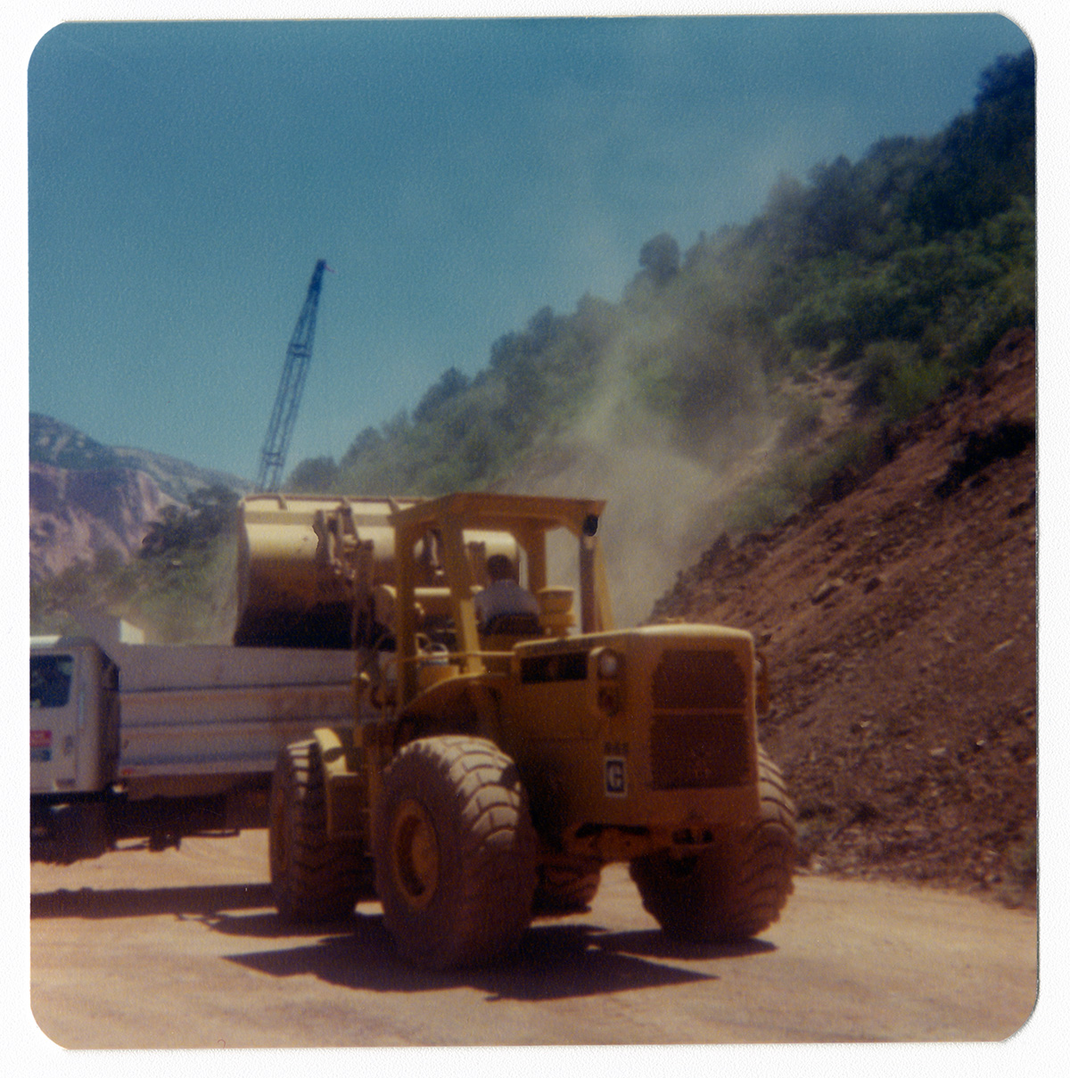 Excavator clearing dirt and rocks into dump truck to repair road in Kolob Canyon.