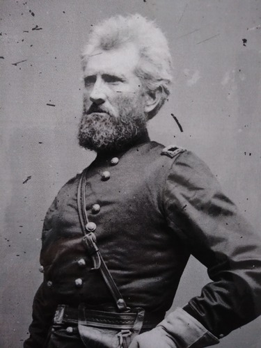 A bearded, white haired army general poses in uniform for a studio portrait.