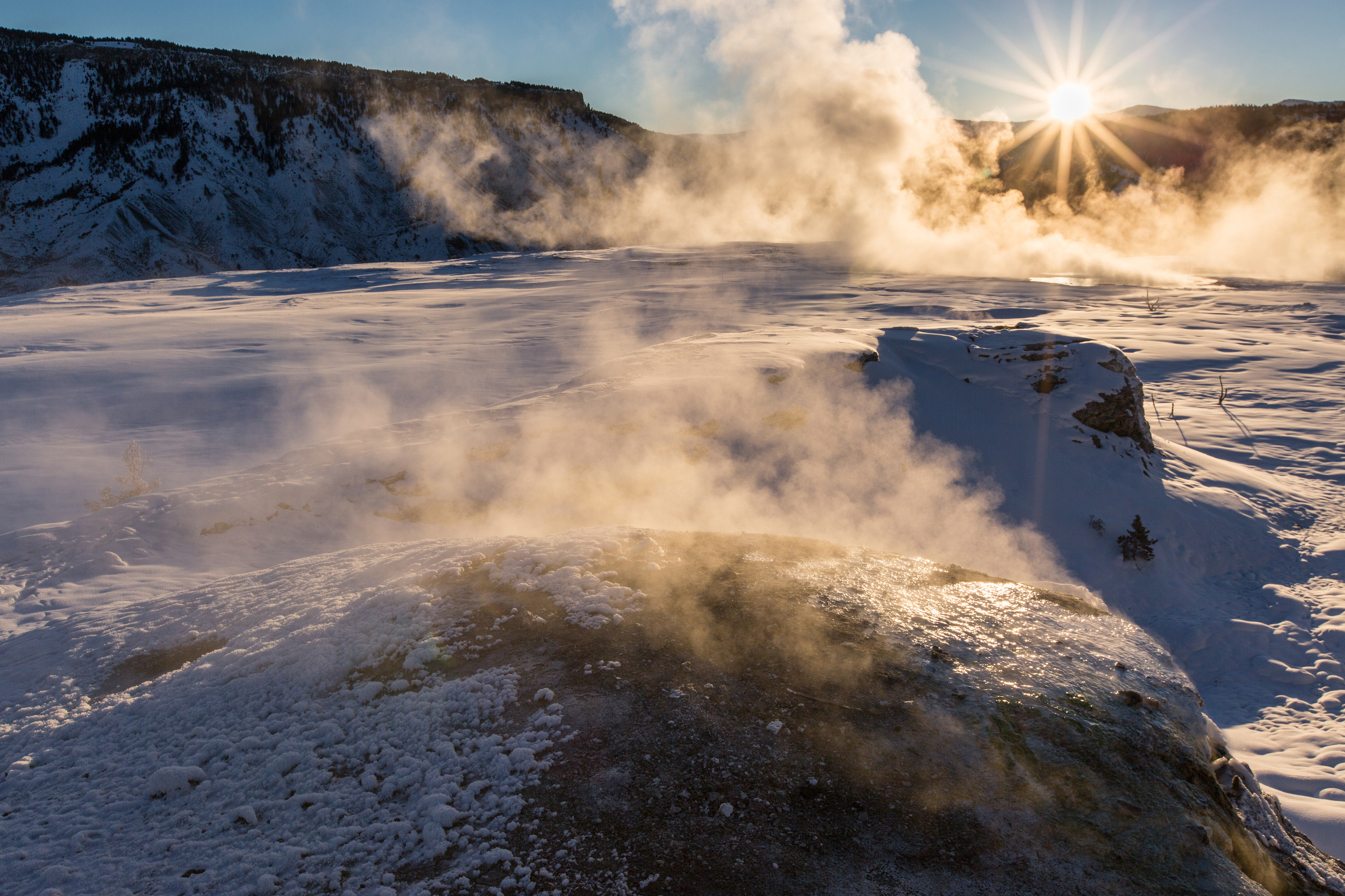 Sun rises behind steam rising from thermal features