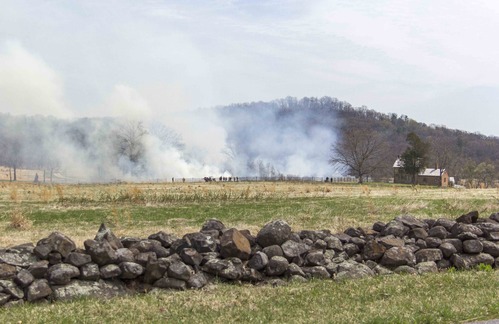 The prescribed fire begins on the northwest corner of the Bushman farm. Prescribed fire workers are seen off in the distance. The Bushman farm is off to the right. A small stone wall is in the foreground. 