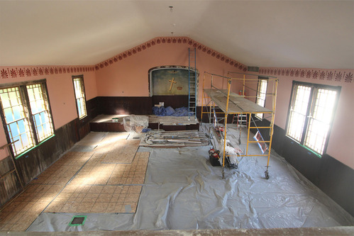 A large rom with pink walls and red stenciling near the ceiling. Scaffolding sits in the center of the room.