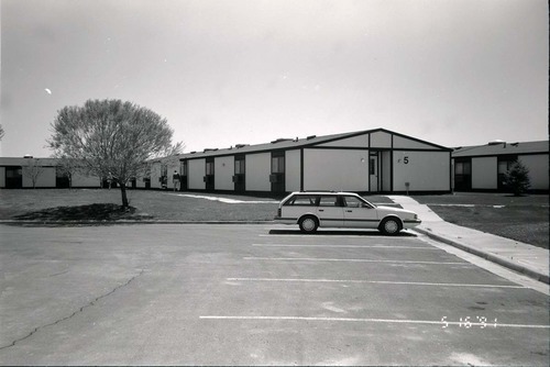 Barracks and parking area with man walking on sidewalk. Building number 5. [Image possibly for comparative housing study]