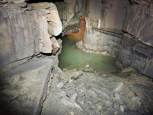 A small greenish body of water in a gray, steep sided cave room.