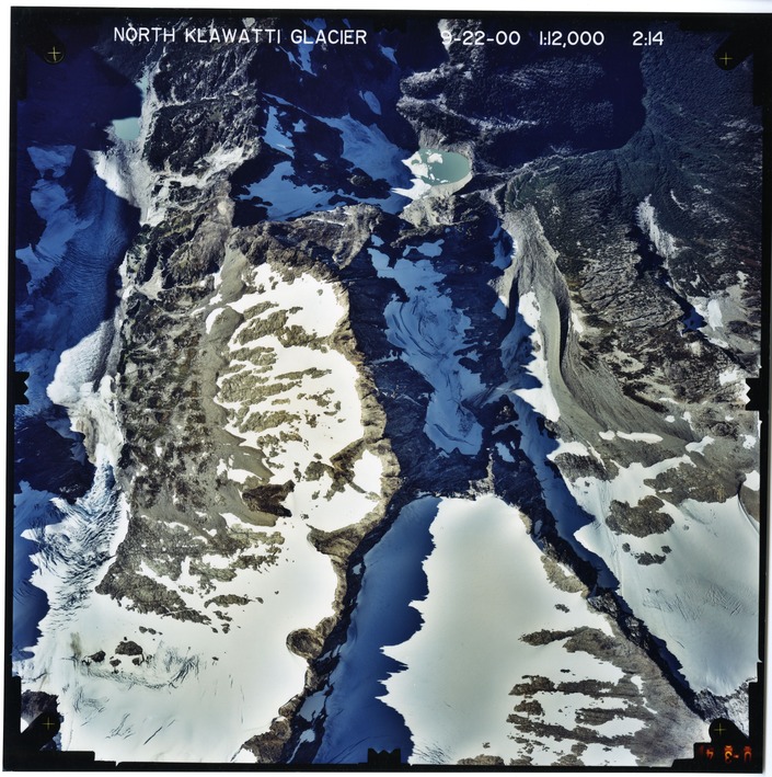 Color aerial photograph of glacier, snowfields, and alpine lake on mountain peak.