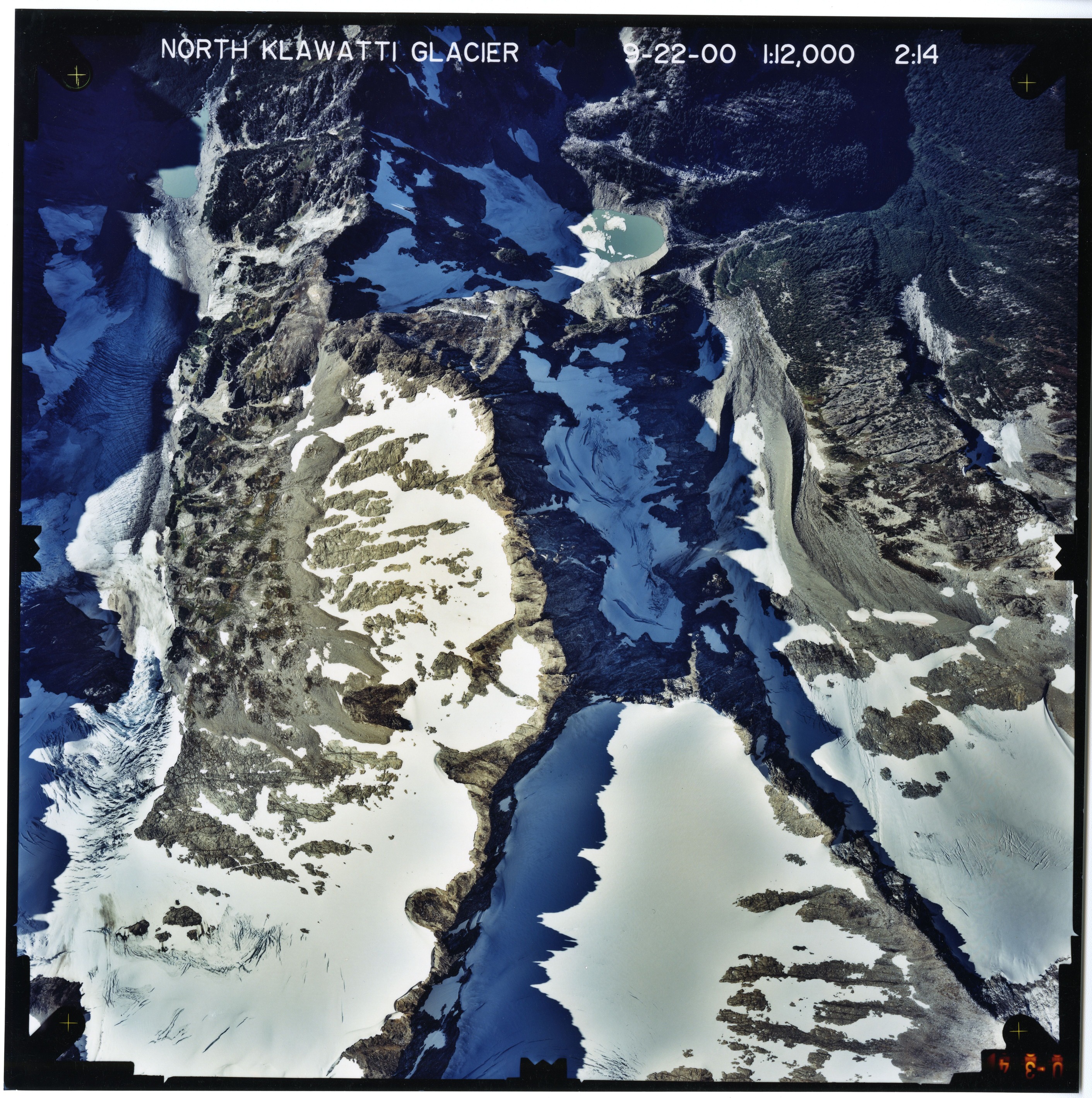 Color aerial photograph of glacier, snowfields, and alpine lake on mountain peak.