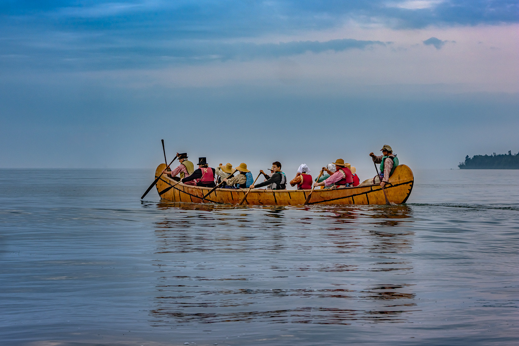 A group of people paddle a large birch bark canoe in the bay.
