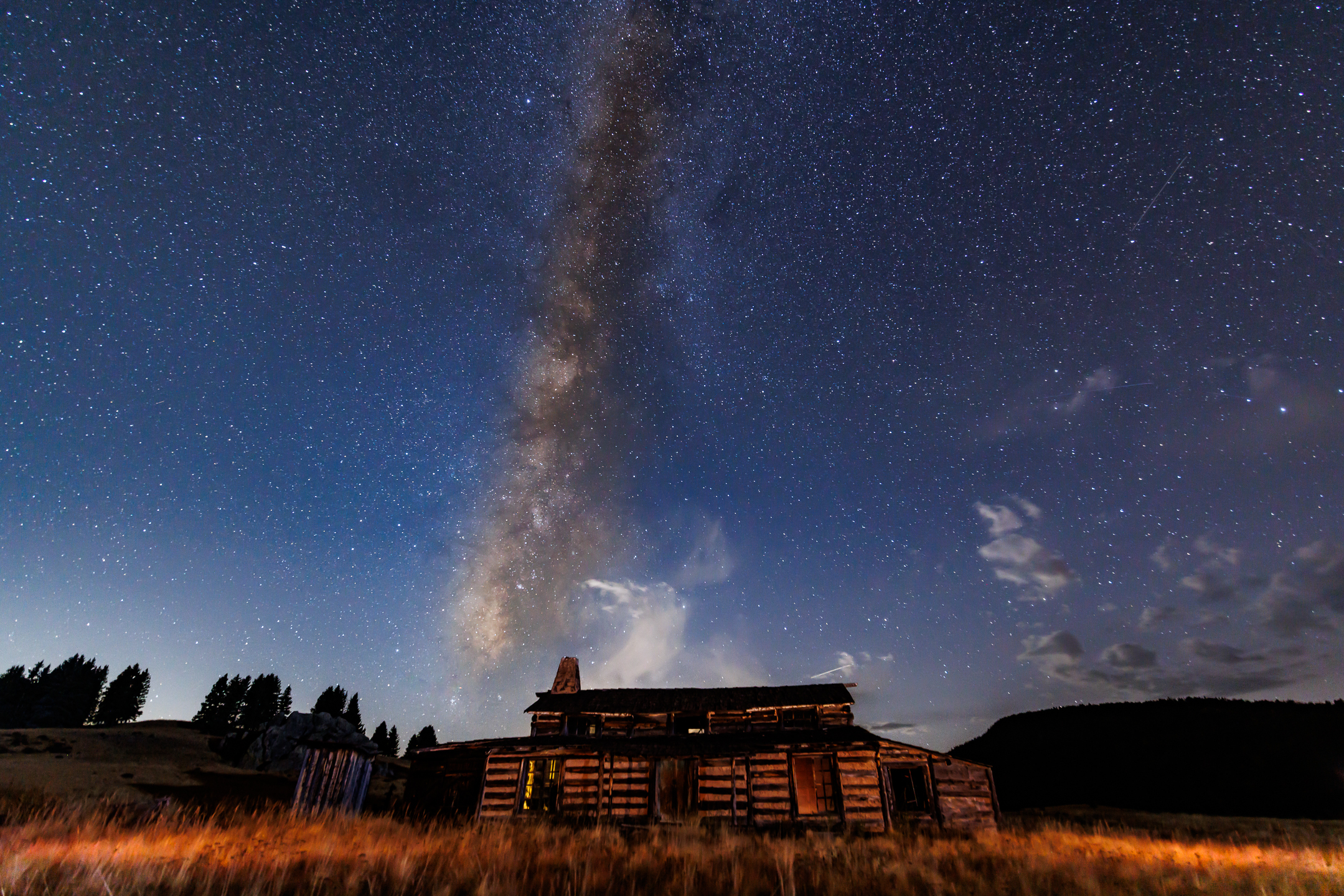 A vertical cluster of stars rises above an old log cabin.