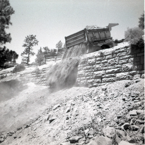 Dump truck dumping dirt over retaining wall during repairs of all along East Rim road.