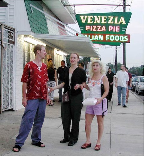 a group of people with take out boxes leave a restaurant with a retro sign, "Venezia PIzza Pie, Italian Foods"