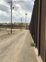 A dirt road next to a border fence.