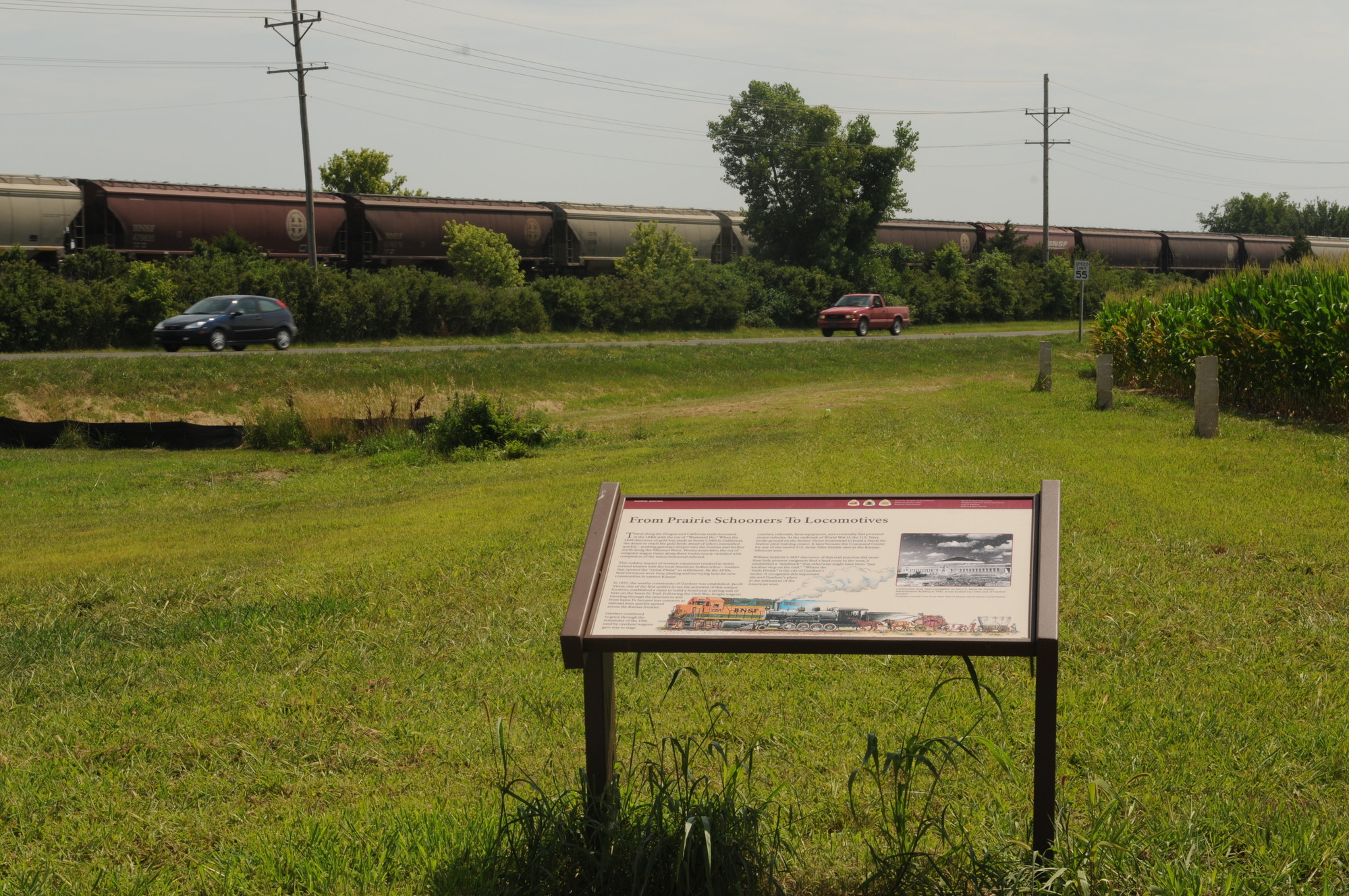 "From Prairie Schooners to Locomotives" wayside with train and cars in the background at Gardner Junction