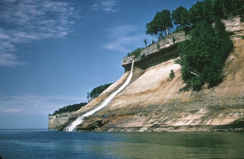 Bridalveil Falls flows vertically over a hard rock cap onto softer sandstone rock that slopes at a 45 degree angle. The water flows into Lake Superior.