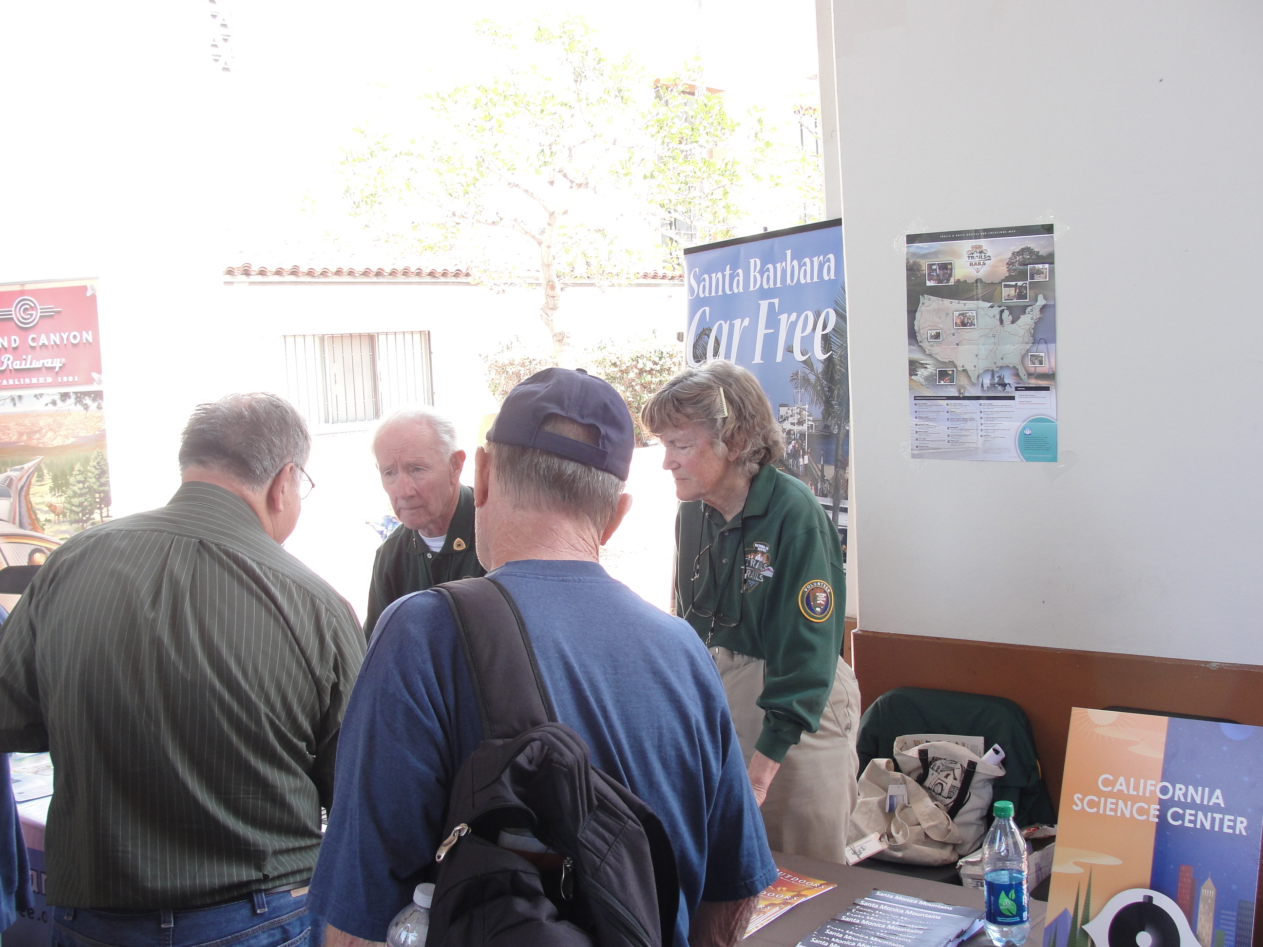 Two NPS volunteers stand behind a table outside speaking to two people