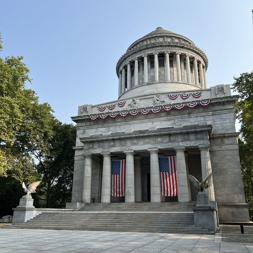 Grant's Tomb adorned with American flags and buntings. There are two eagle statues in front on either side of the entry stairs.