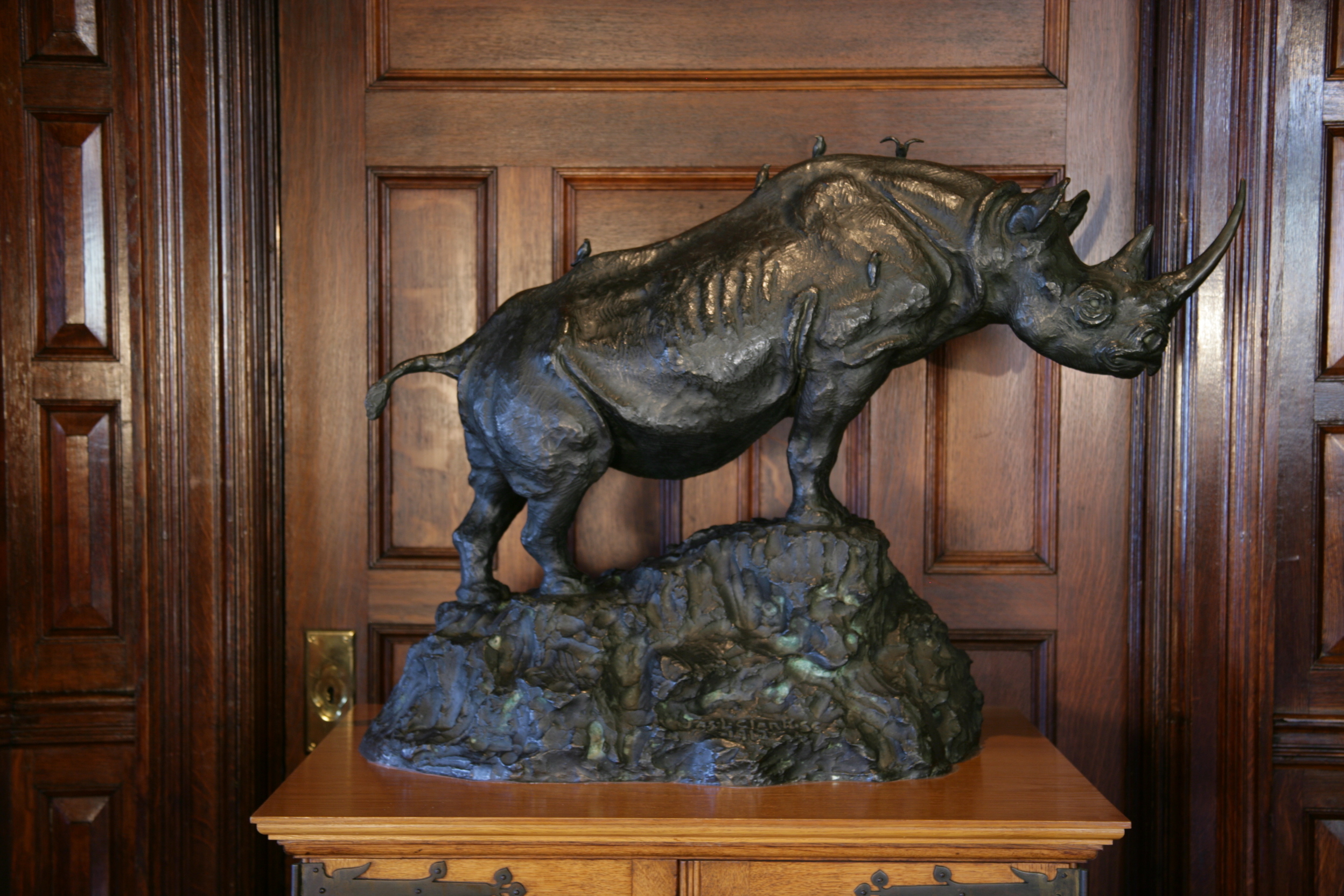 A large bronze sculpture of a rhinoceros on a peak, with small birds sitting on its spine. 