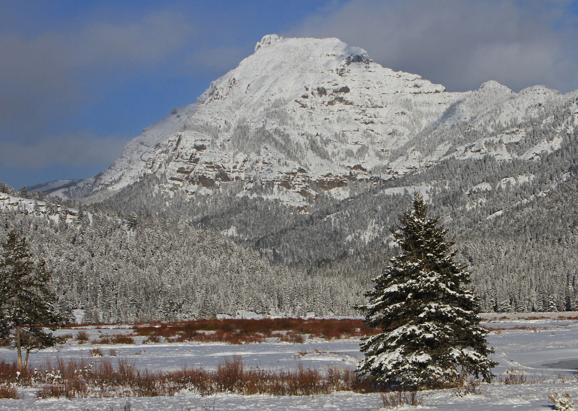 A snow covered peak sits behind a flat snow covered flat.