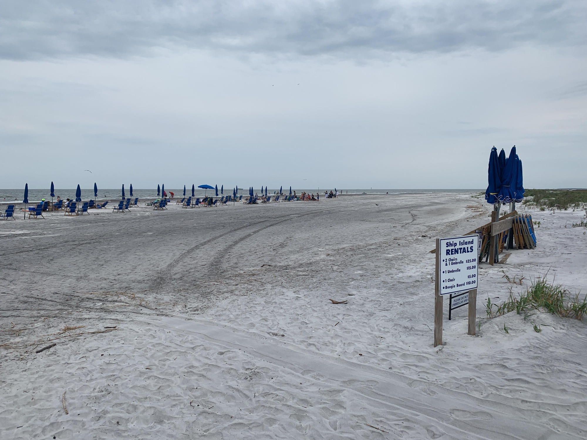 White sand beach with blue umbrellas and chairs. Grey sky and blue water in the background.