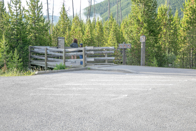 A woman and boy stand at a trailhead sign at the beginning of a boardwalk.