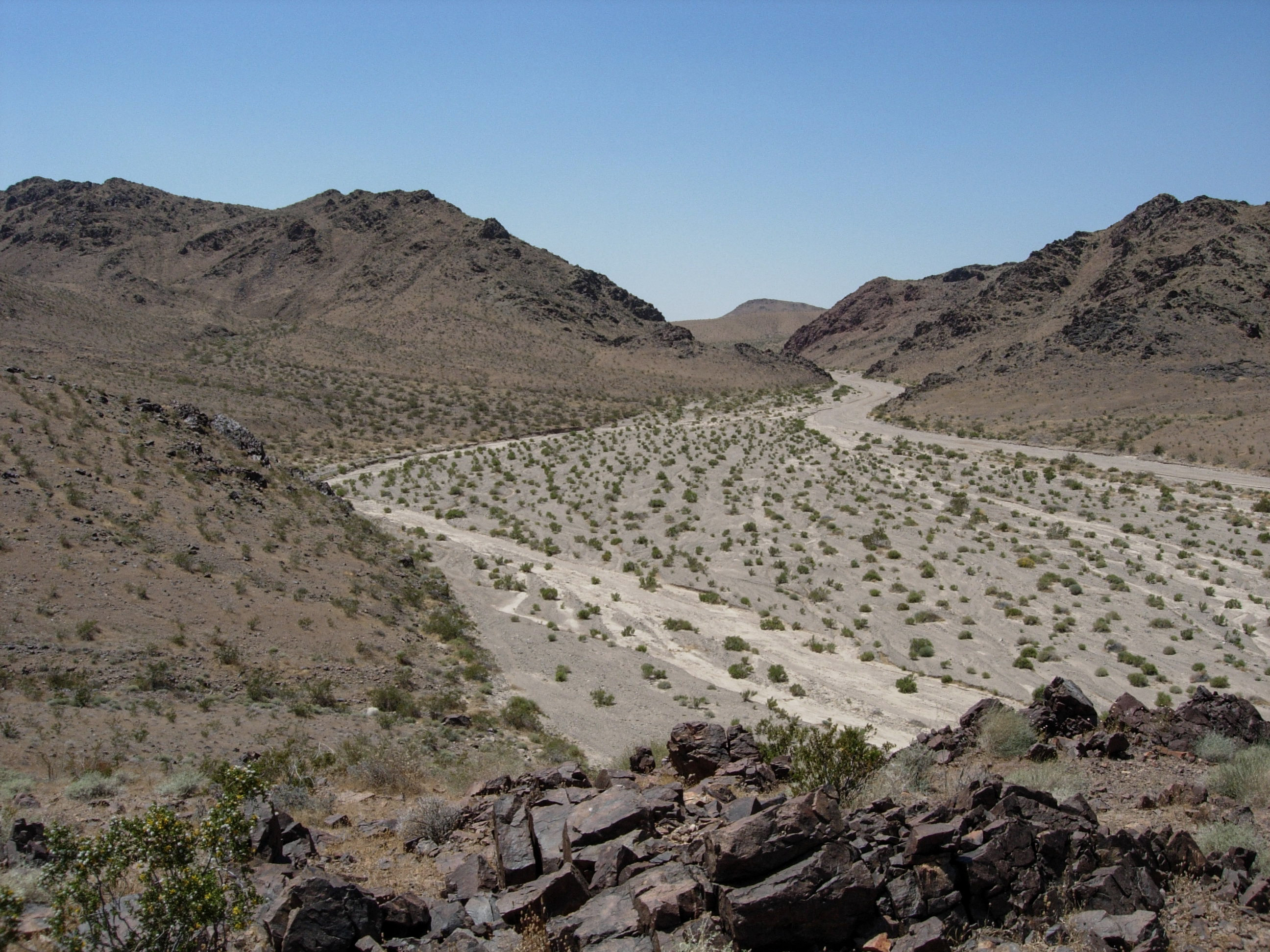 Looking down upon a desert wash. The wash narrows as it climbs between two desert mountains in the distance.