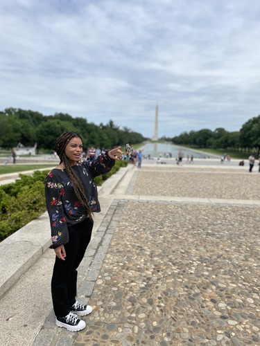 Woman smiling and pointing at something, with a reflecting pool and the Washington Monument in the background. 