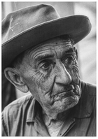 Historic black and white portrait of an old man wearing a hat showing deep wrinkles in his face.