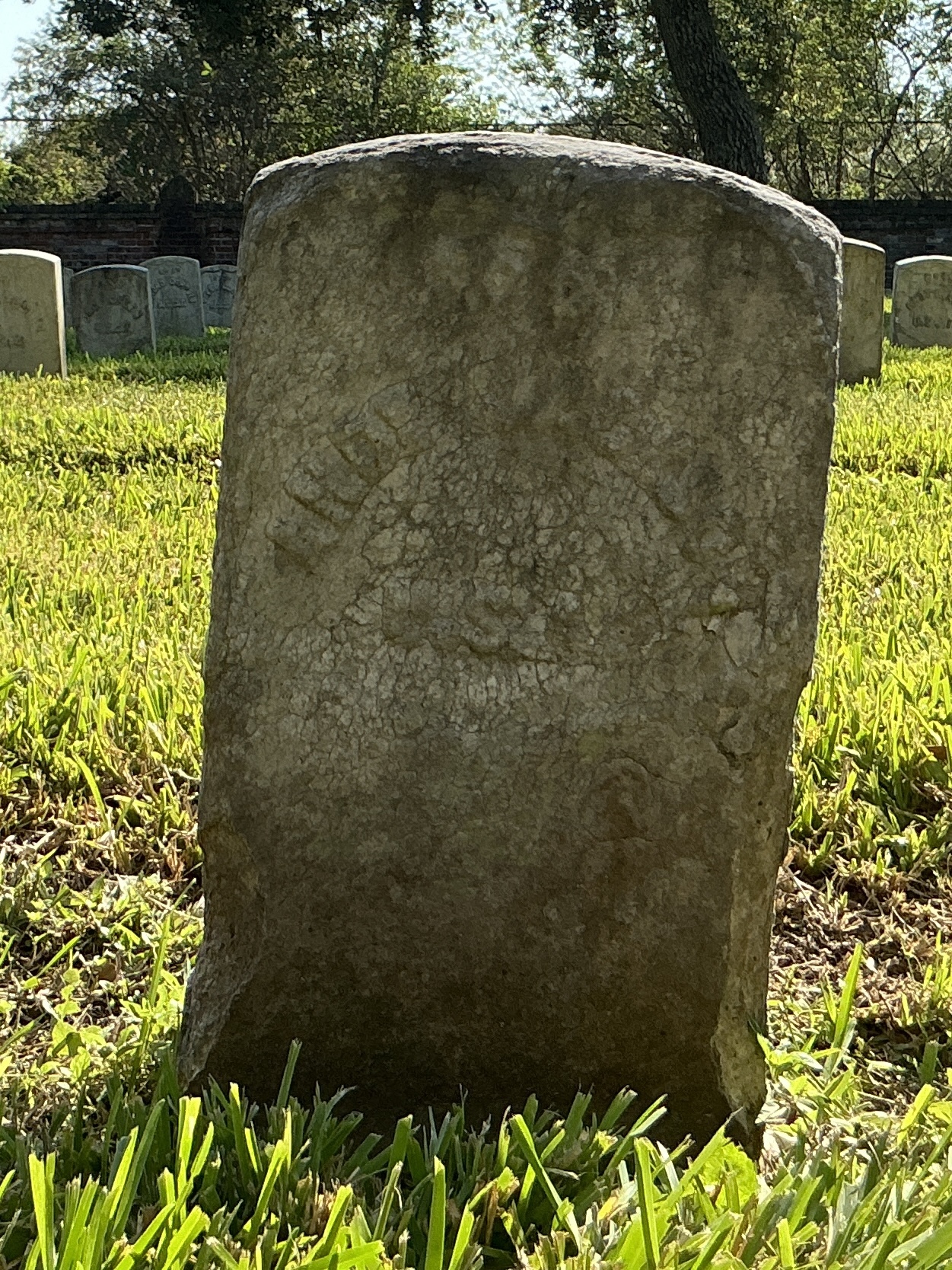 Front of historic upright marble headstone with recessed shield with recessed lettering face.