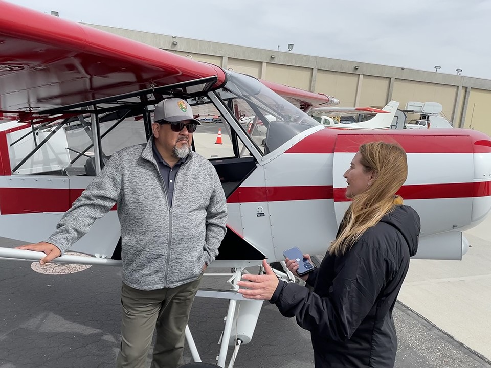 NPS aircraft specialist, Kristin Swoboda, briefs director, Chuck Sams, next to a parked plane.