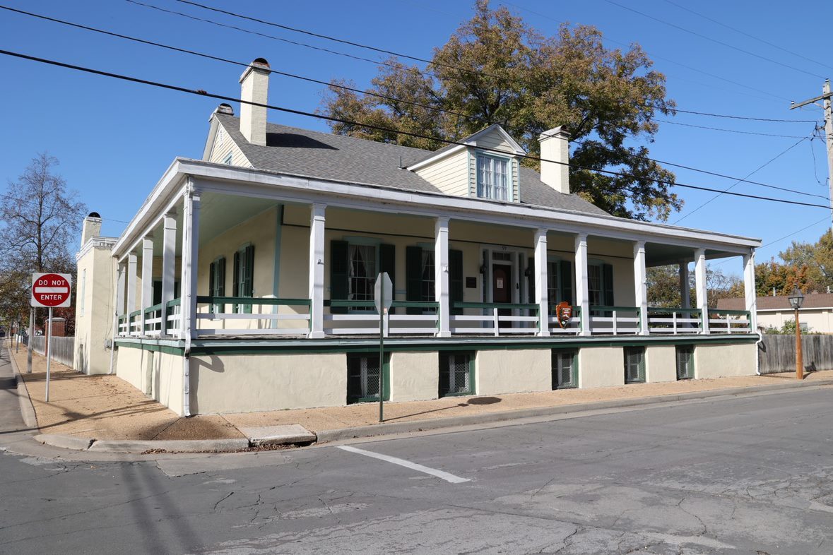View of a two story cream colored house with a wrap around porch from the street. 