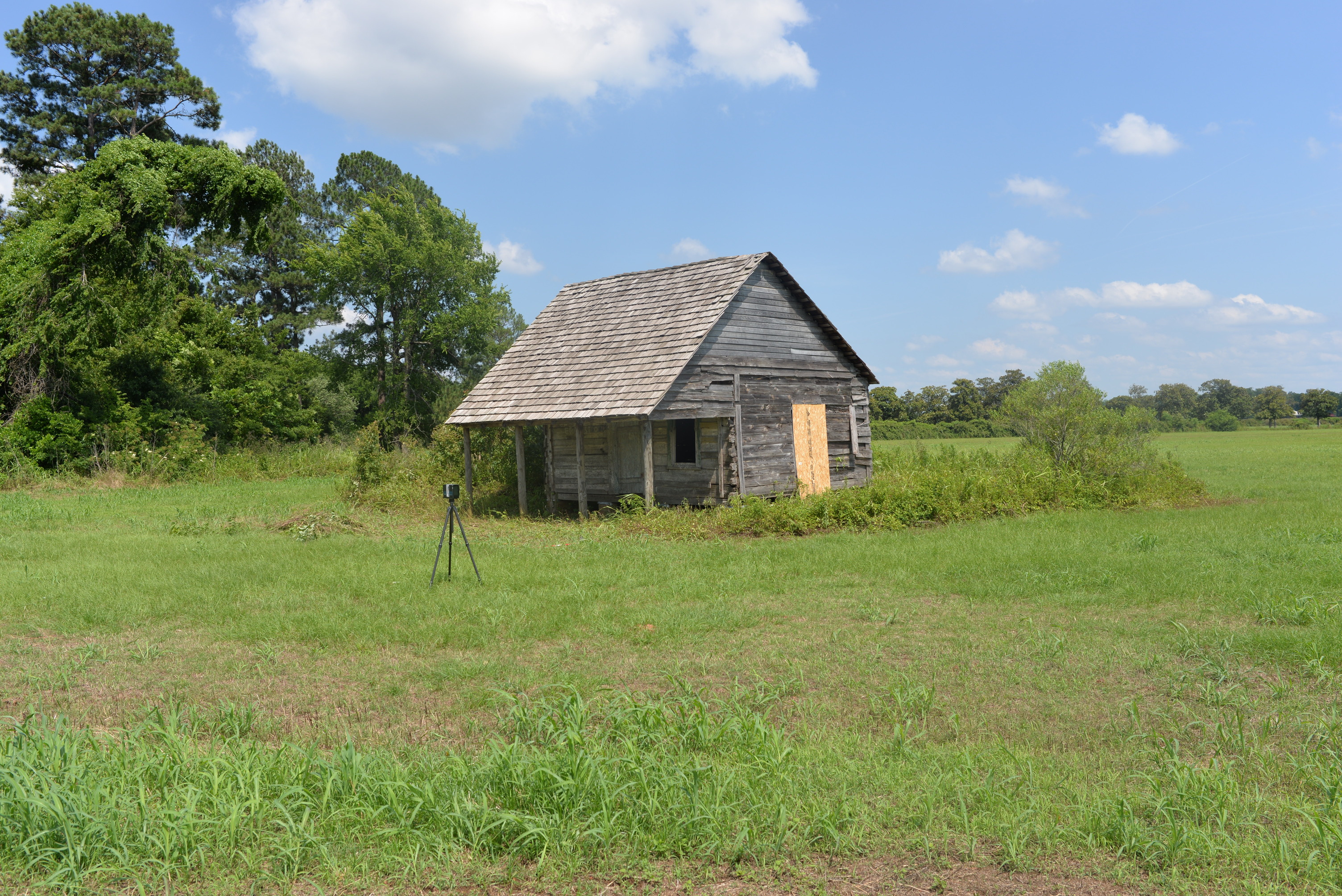 Wide view of wooden structure sitting in the middle of a field, a laser scanner is positioned towards the front.