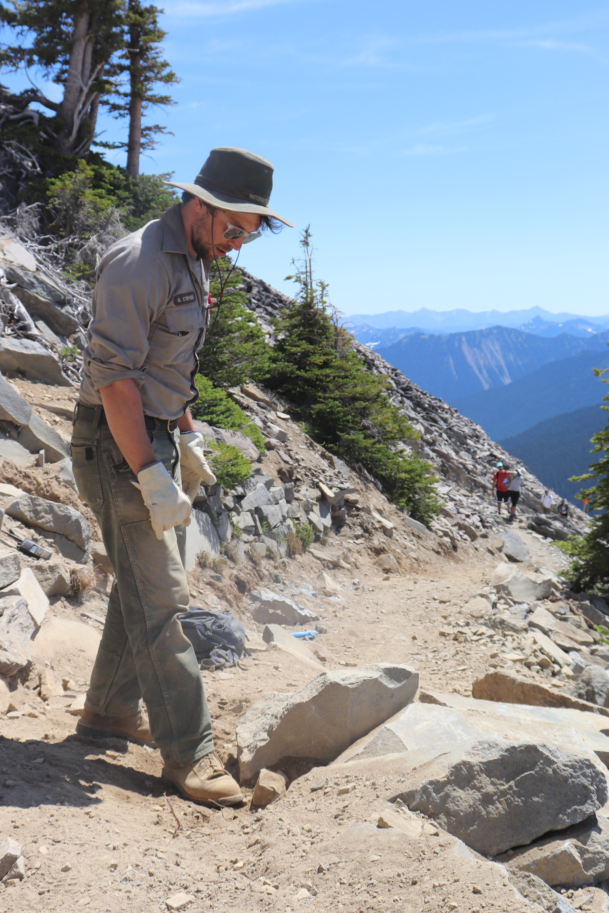 A park employee prepares to move a rock at his feet on a dirt trail.