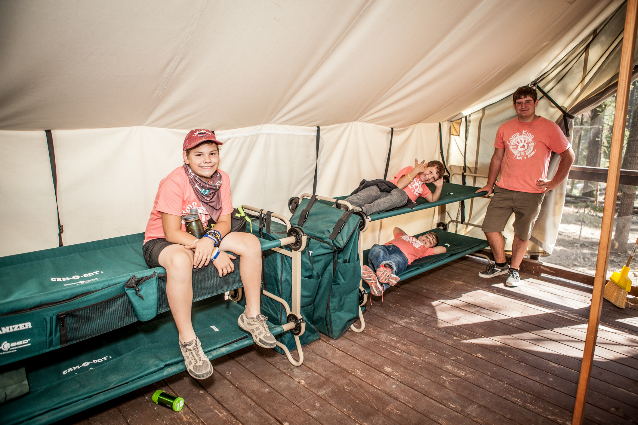 Four boys pose for a photo on green, canvas, stacked cots in a tan canvas camping cabin.