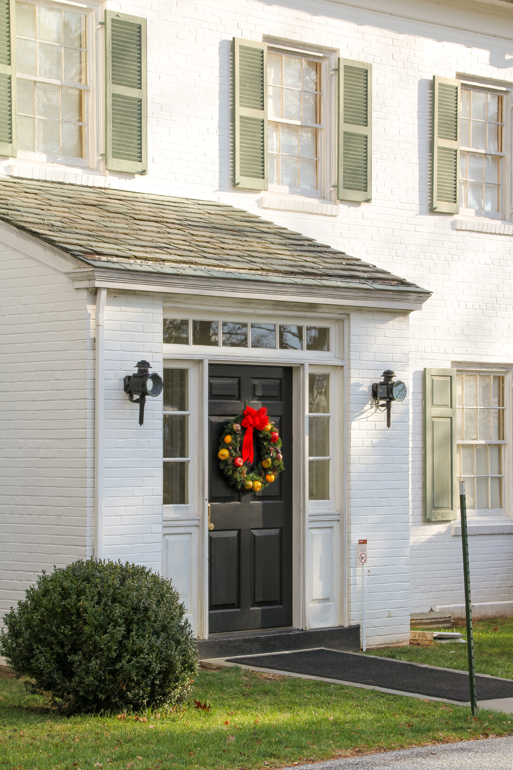 A white brick house with a small entry way with a wreath hanging on a brown wooden door.