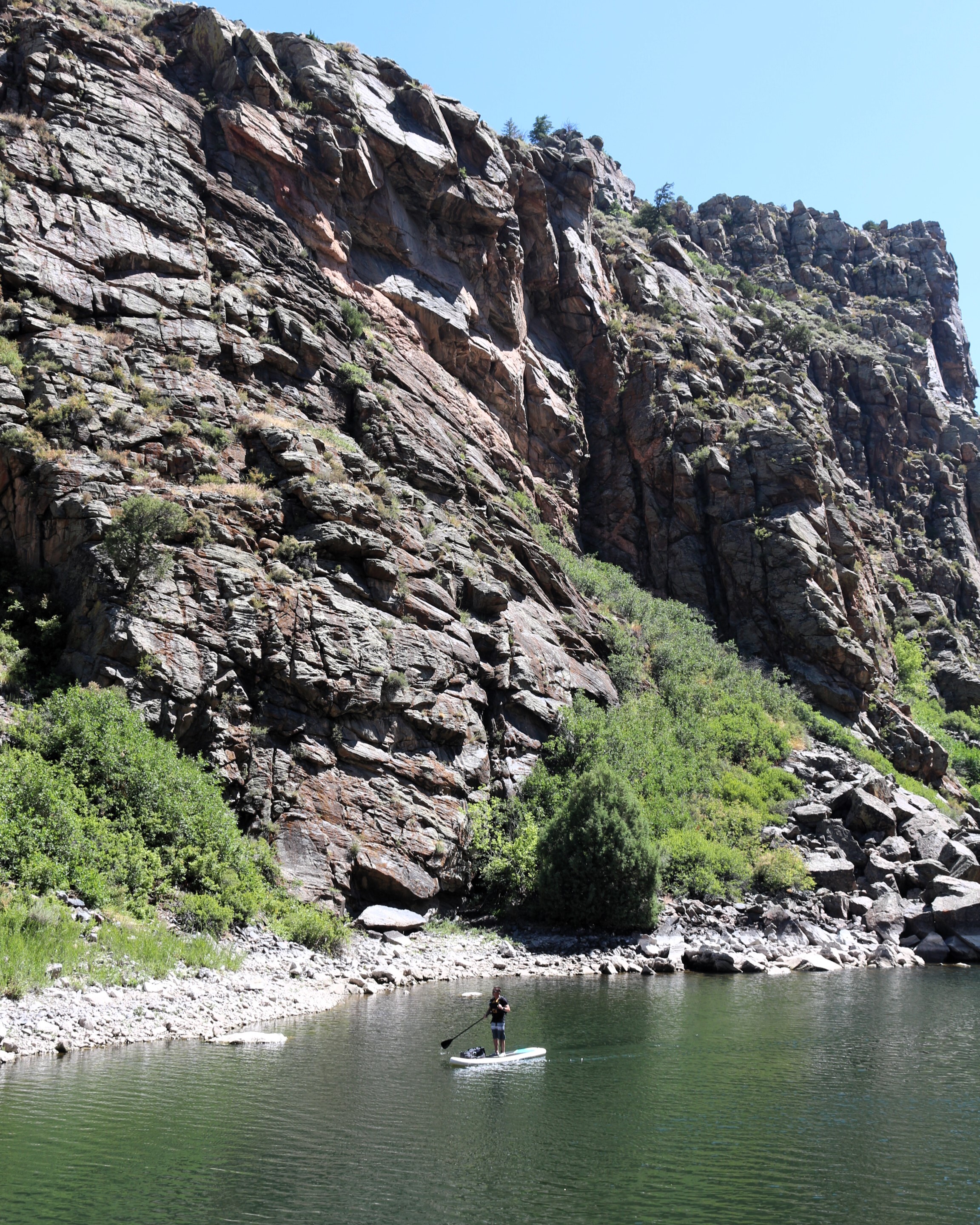 A person paddles on a SUP along a narrow section of a reservoir with steep canyon walls