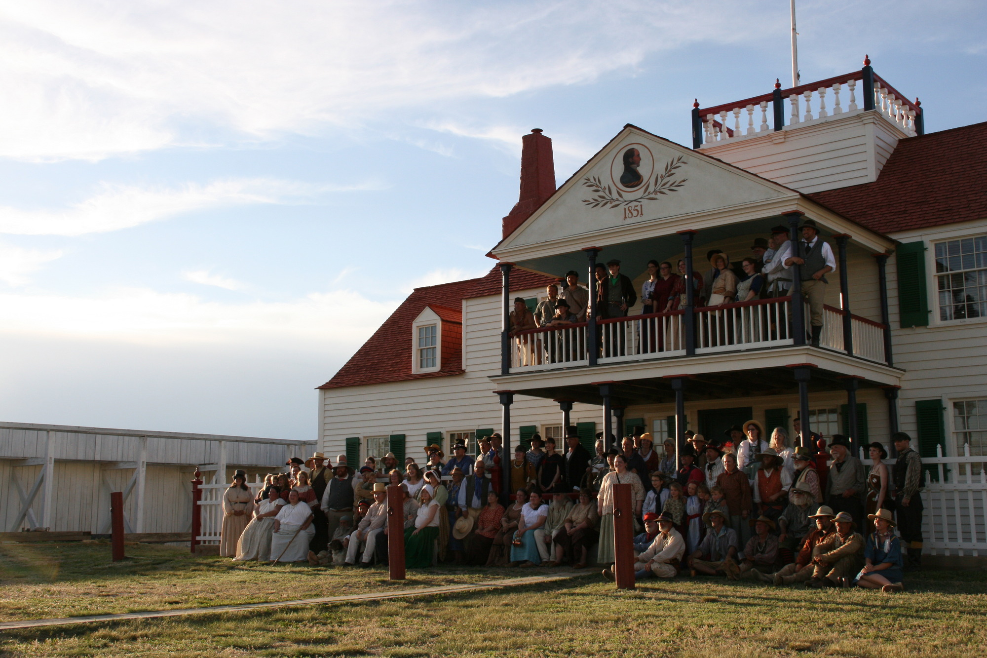 Many people in living history clothing posing in front of a impressive house