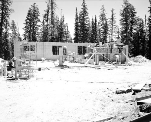 Men laying cinder blocks during construction of utility and maintenance building. Scaffolding with supplies and equipment set up along partial walls.