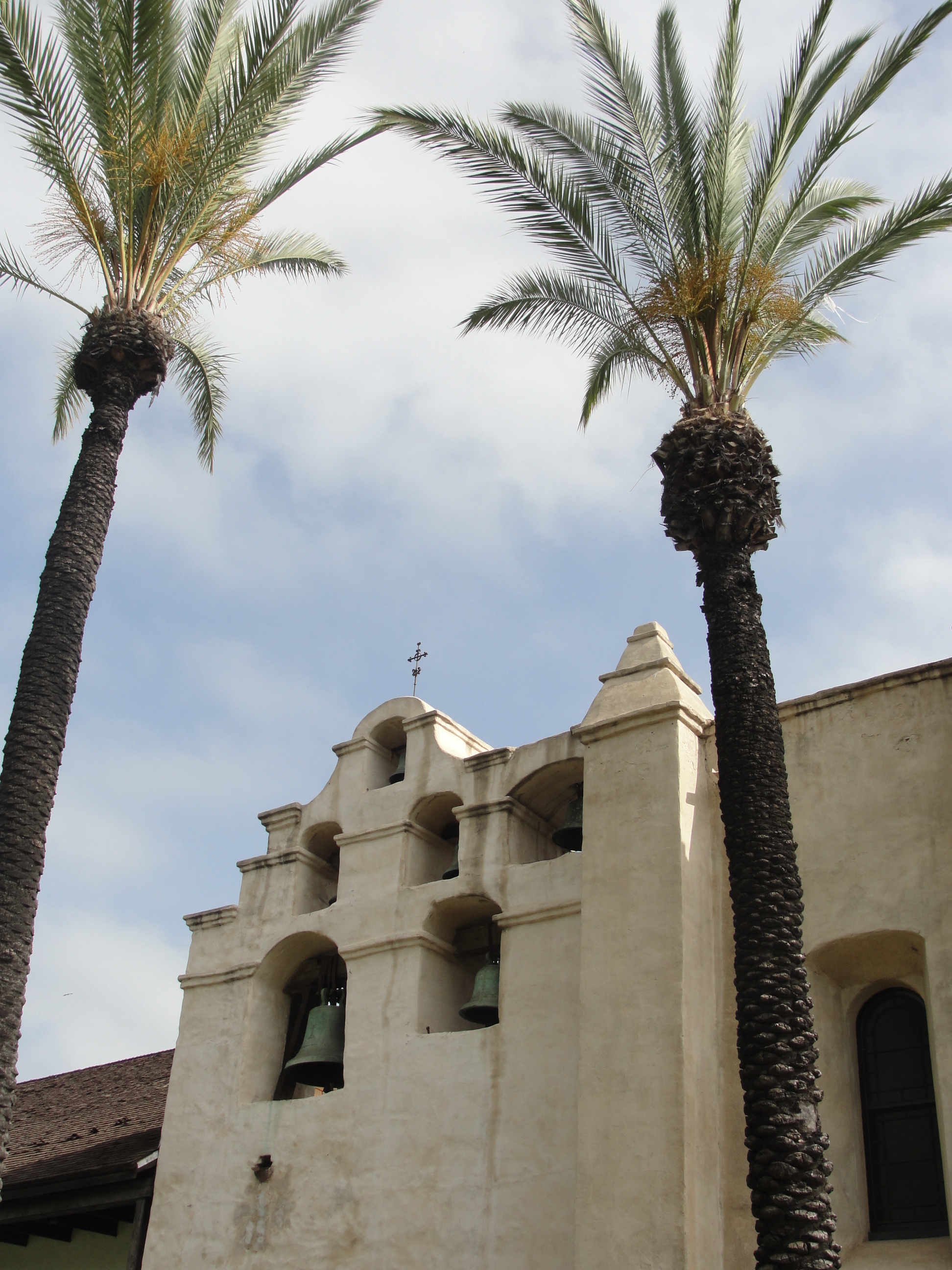 Two palm trees stand in front of a white stucco tower with six bells