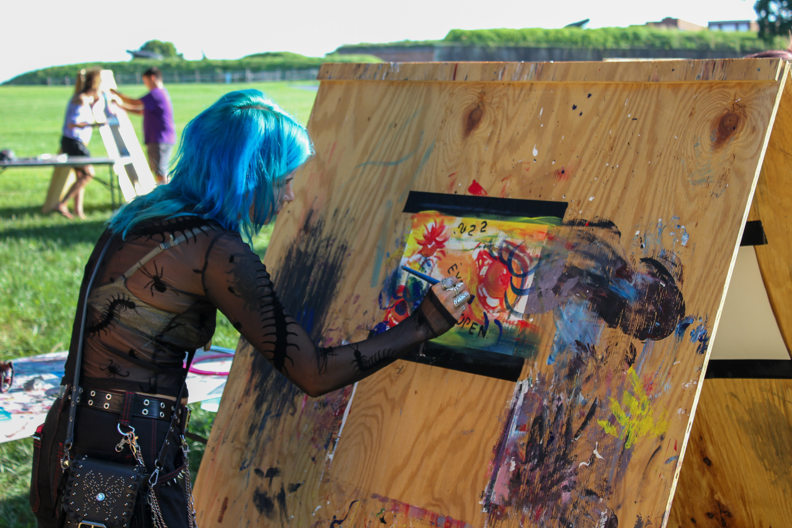 Woman painting on canvas attached to large outdoor easel. 