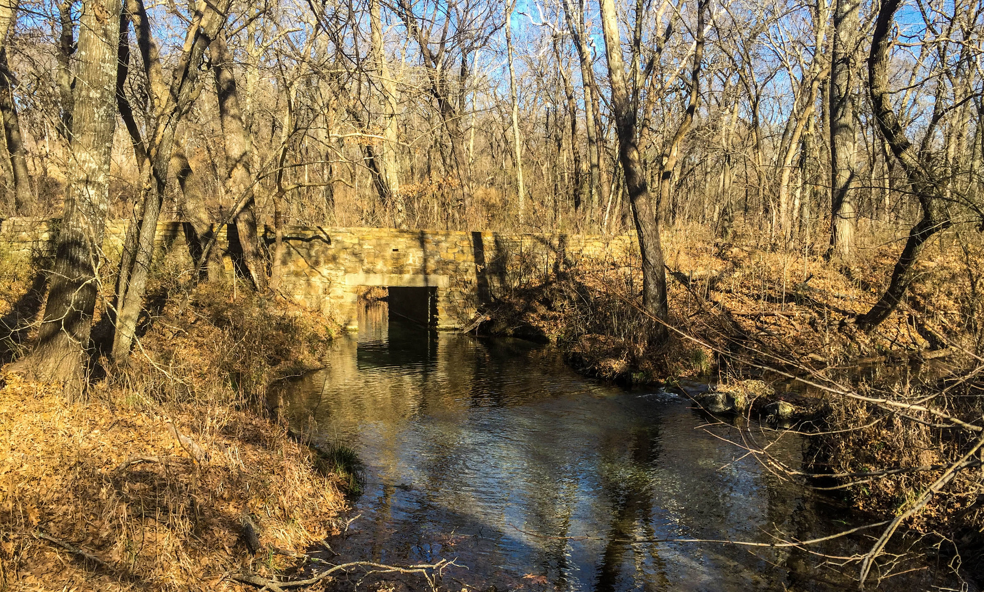 Stone bridge over water Creek in woods bare of foliage during winter