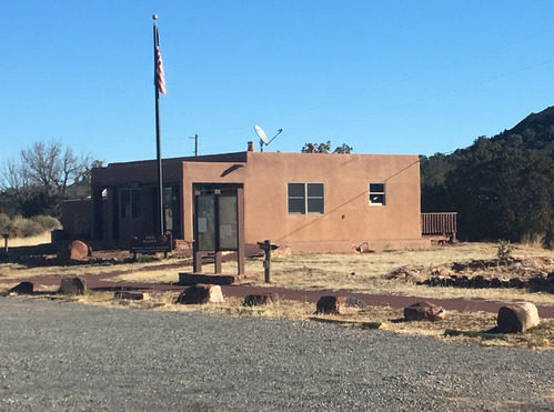 A square building with a tan stuccoed exterior next to a gravel parking lot