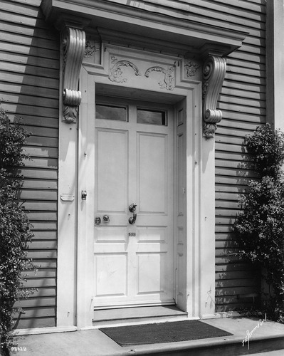 Close up of large front door of old house, with symmetric decorations above. Black and white photo.