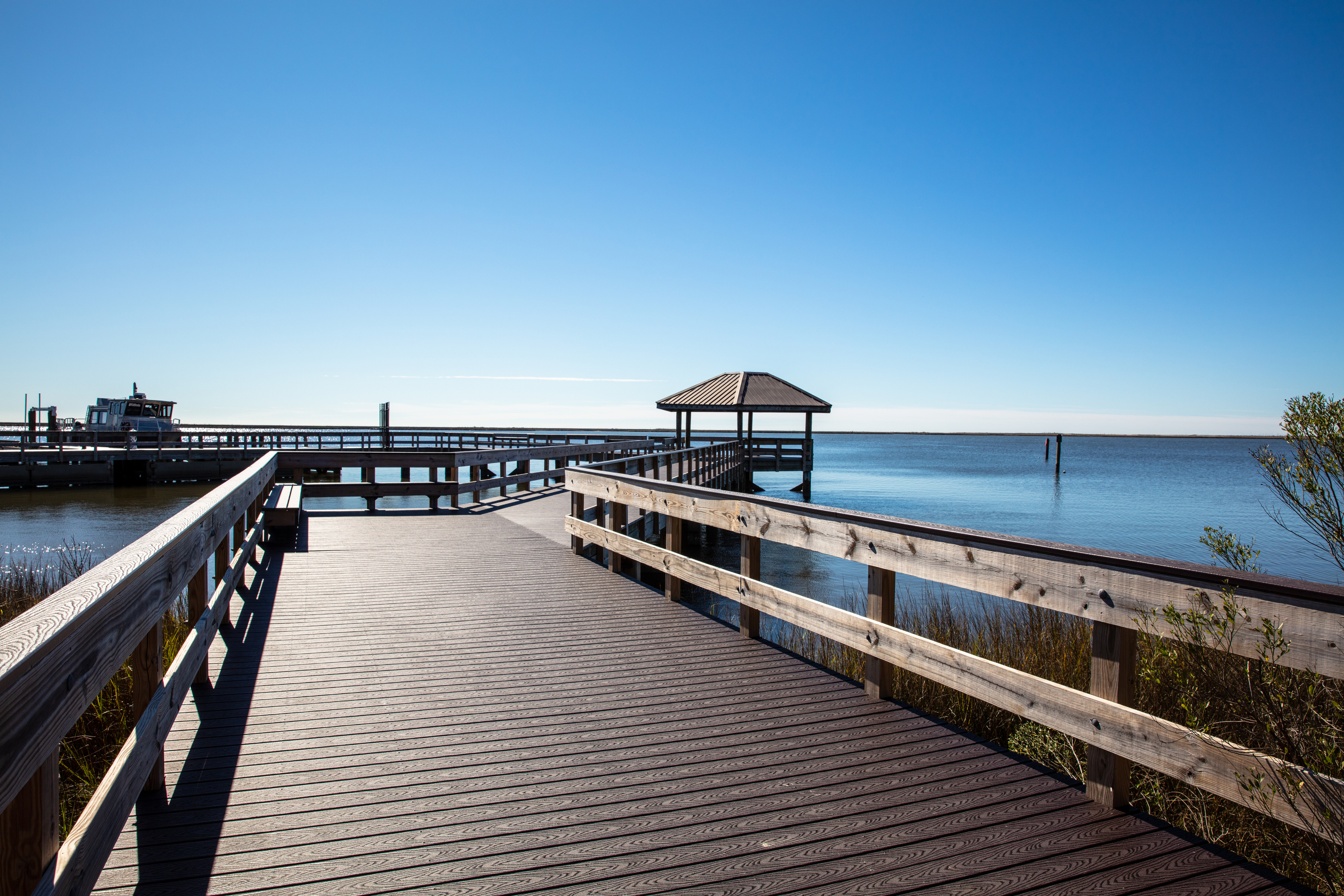A wooden fishing pier and boardwalk stands over still blue water.