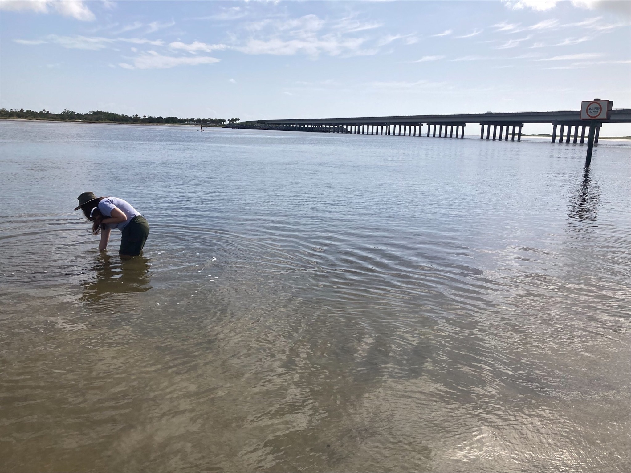 person bends in water bridge in distance 