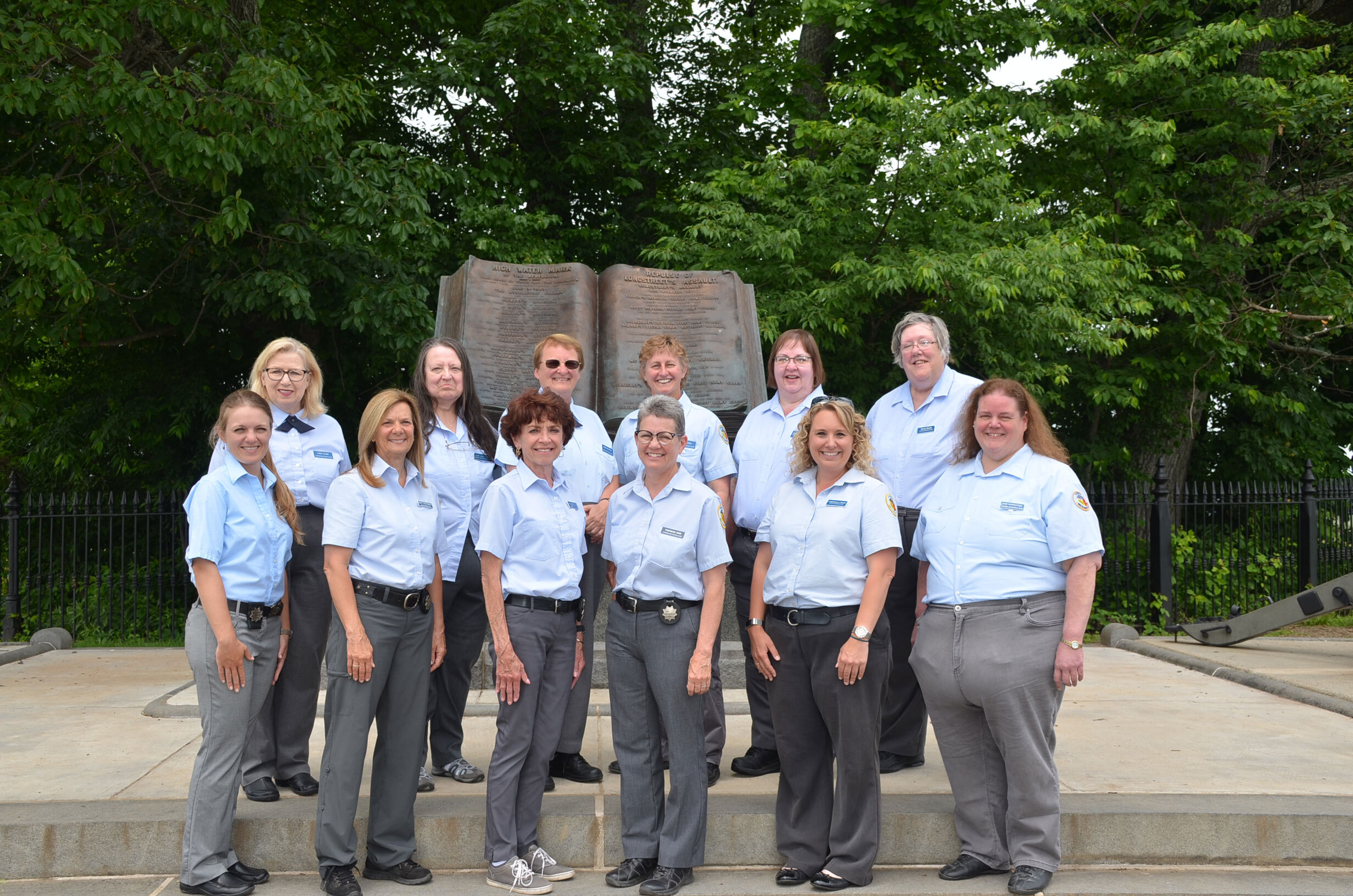 Twelve women guides pose for a group photo wearing their guide uniforms of gray slacks and light blue shirts. Some women are wearing star-shaped guide badges.