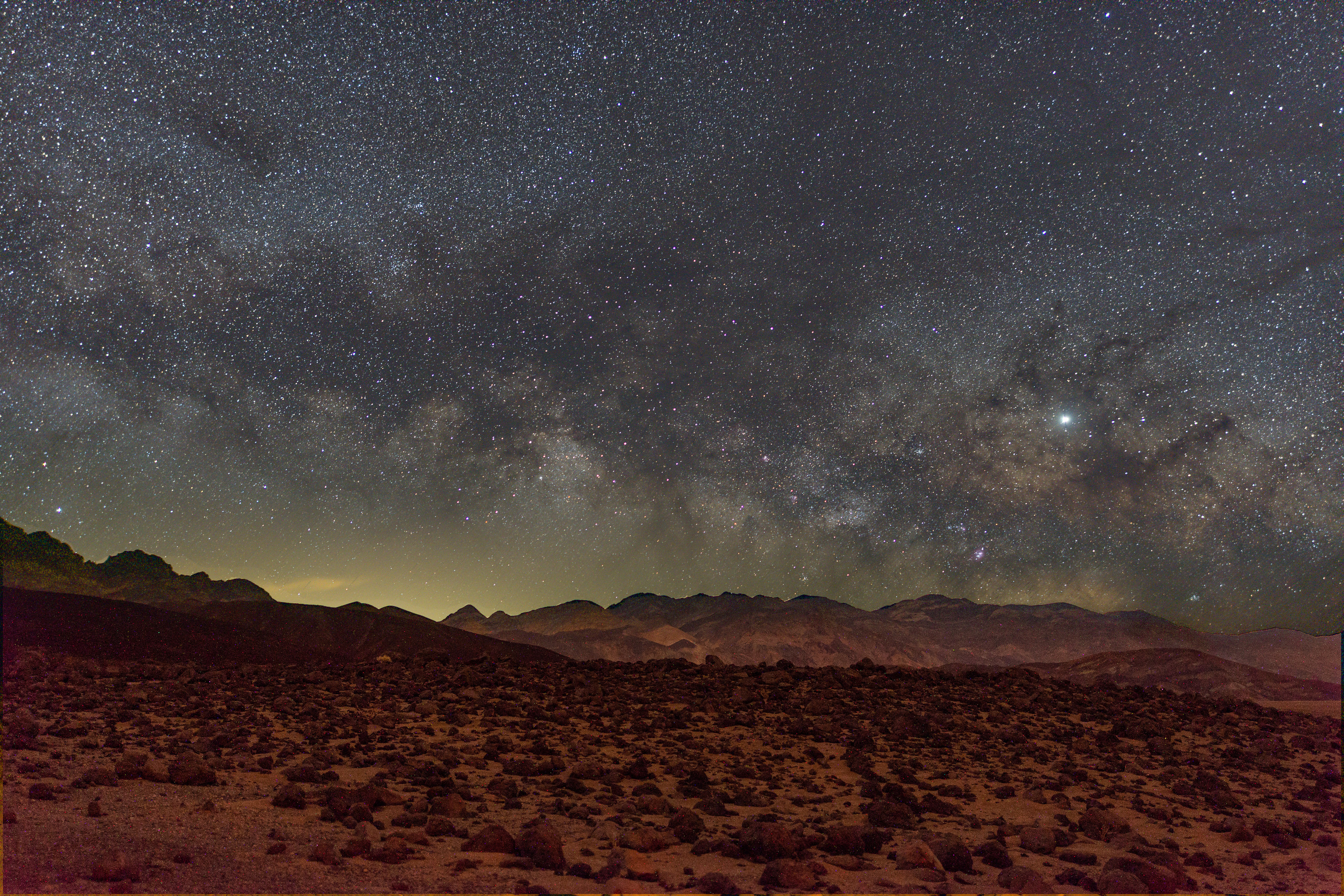 A rocky plain underneath a sky with numerous stars.