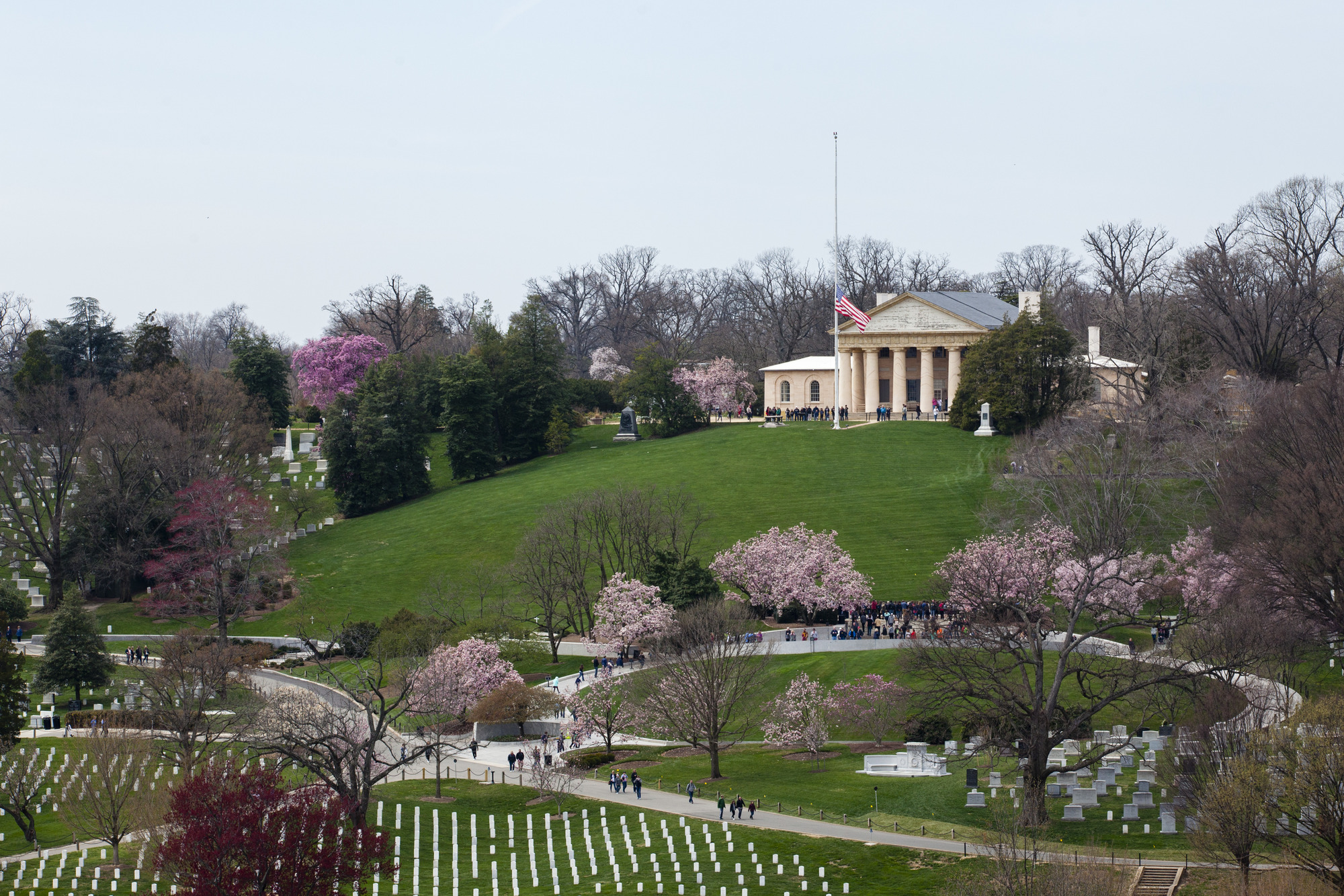 An aerial view of Arlington House in the spring time. Cherry blossom trees are in bloom and the flag is at half mass.