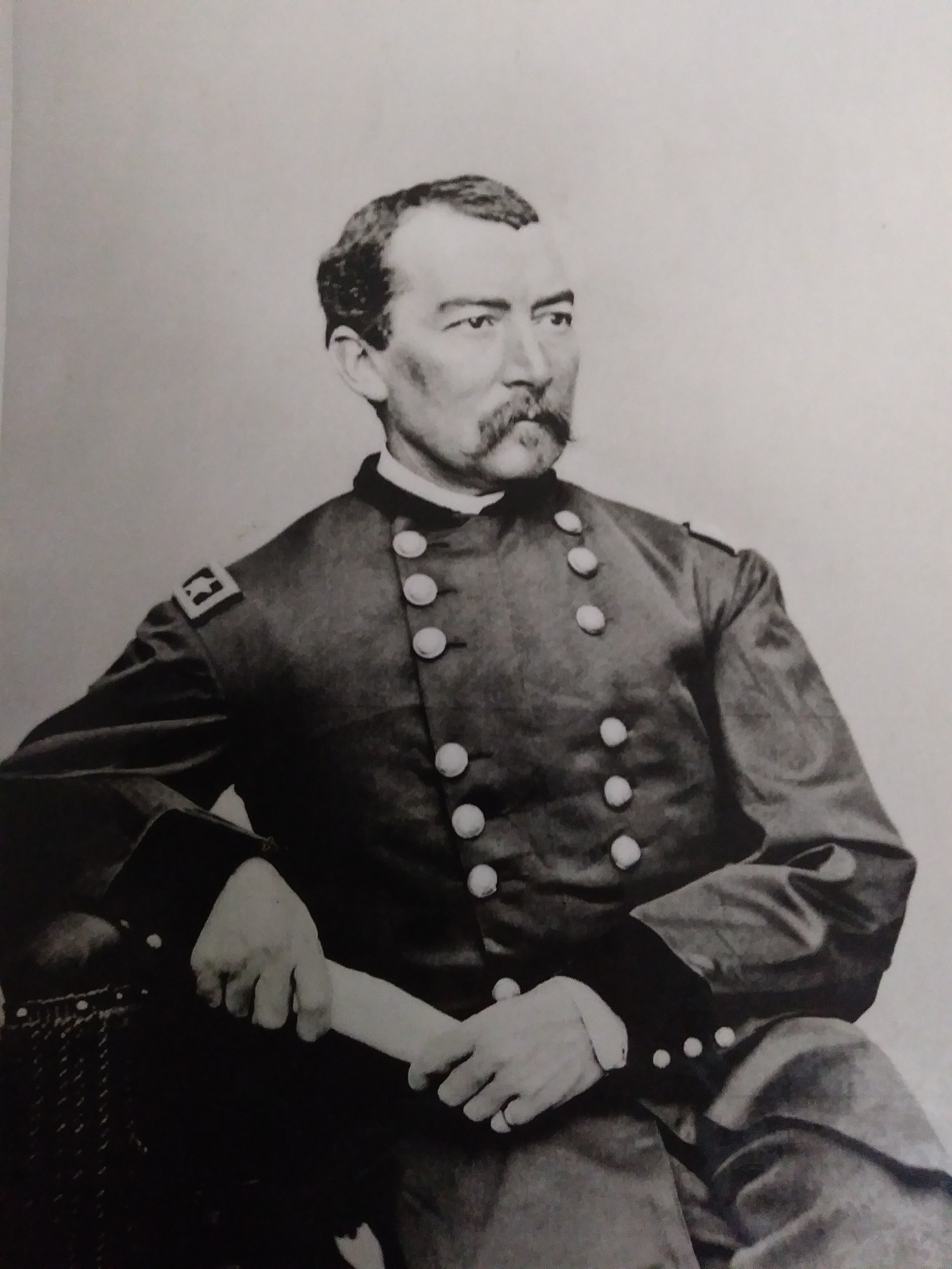 A young, mustached army general in uniform sits for a portrait photo in the 1860s.