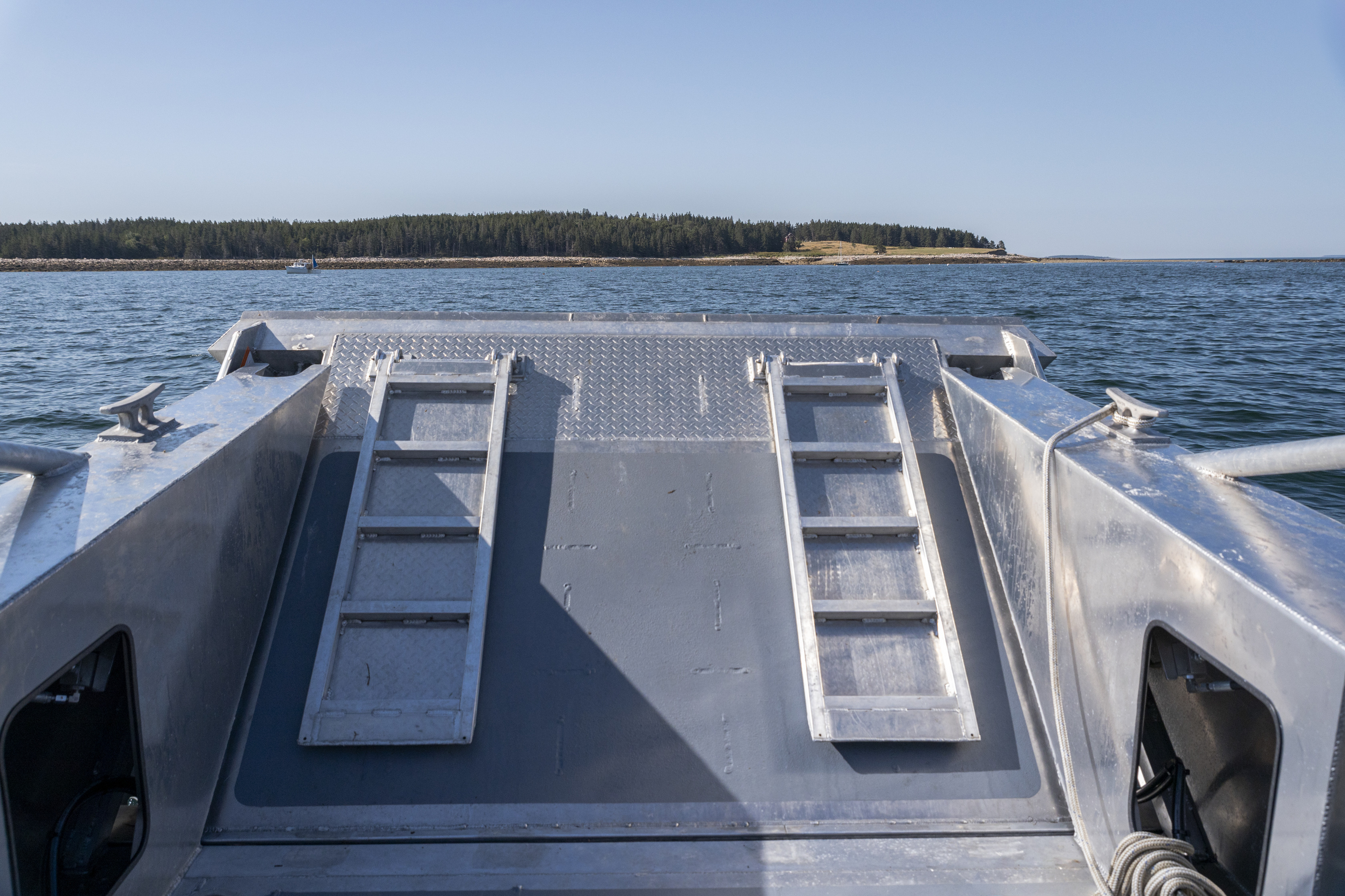 View from the bow of a metal boat approaching Baker Island on a calm blue sea under a clear sky.