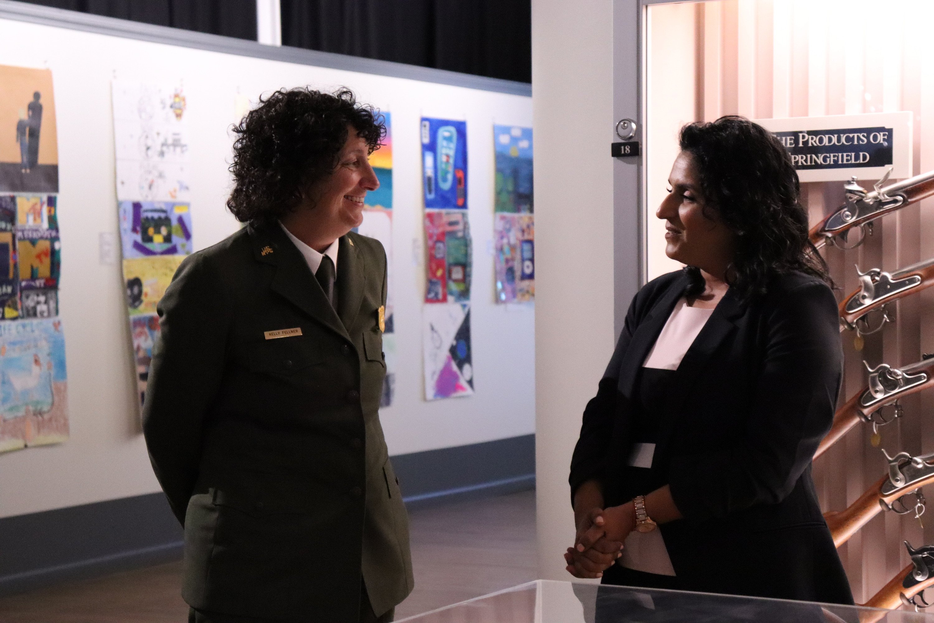 Two individuals stand and talk to each other. 