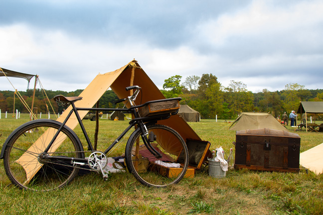: A vintage bike in front of a small tent and a box in a field