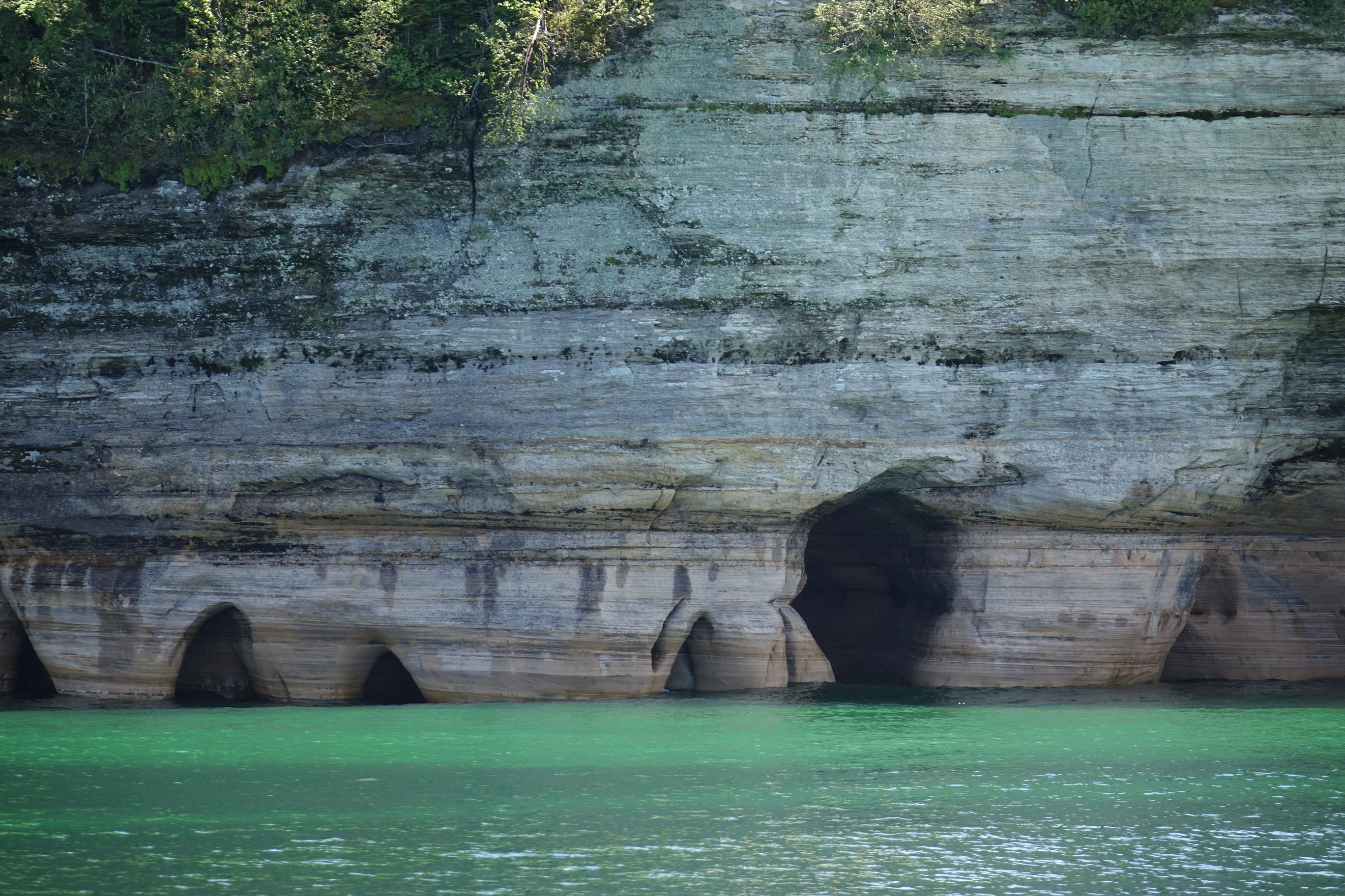 The base of Miners Castle at the water level of Lake Superior. The sandstone layers run horizontal. The rock is eroded into little holes and caves and deep crack.